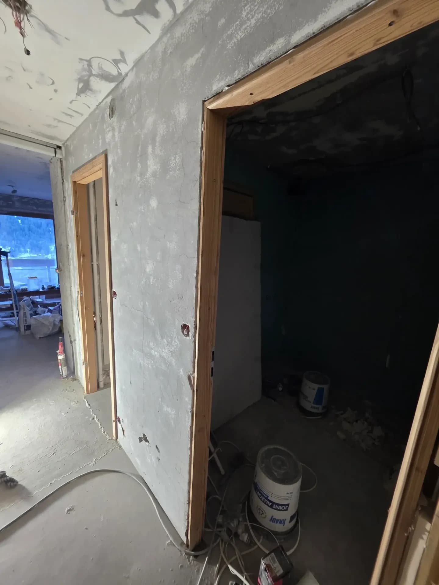 Couloir en rénovation avec murs gris, montants de portes en bois.