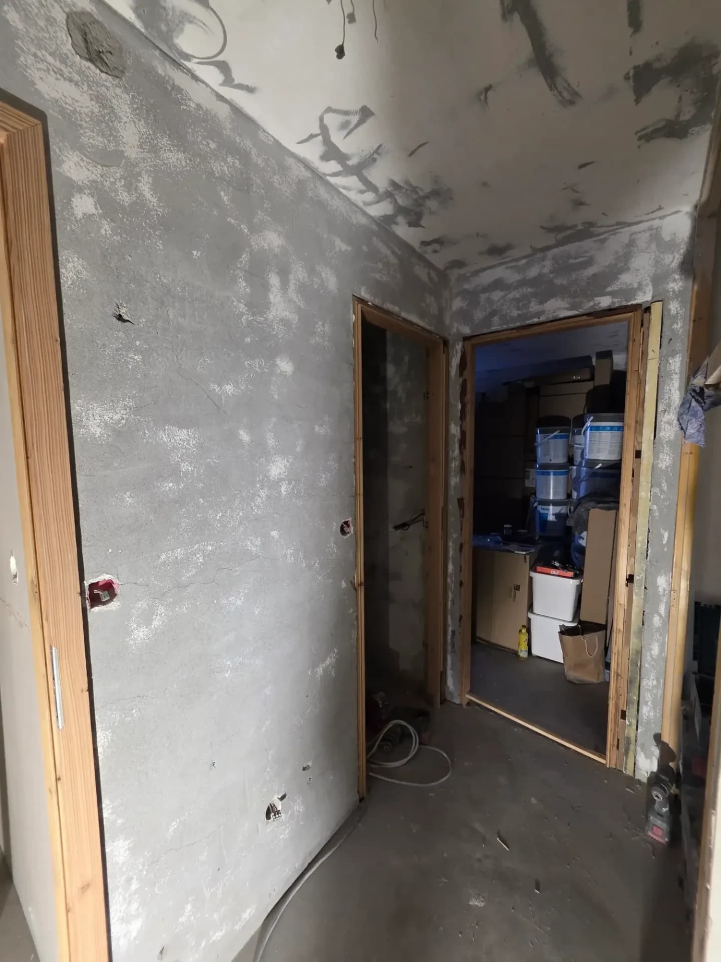 Couloir en rénovation, murs nus gris, dormants de portes en bois mélèze.