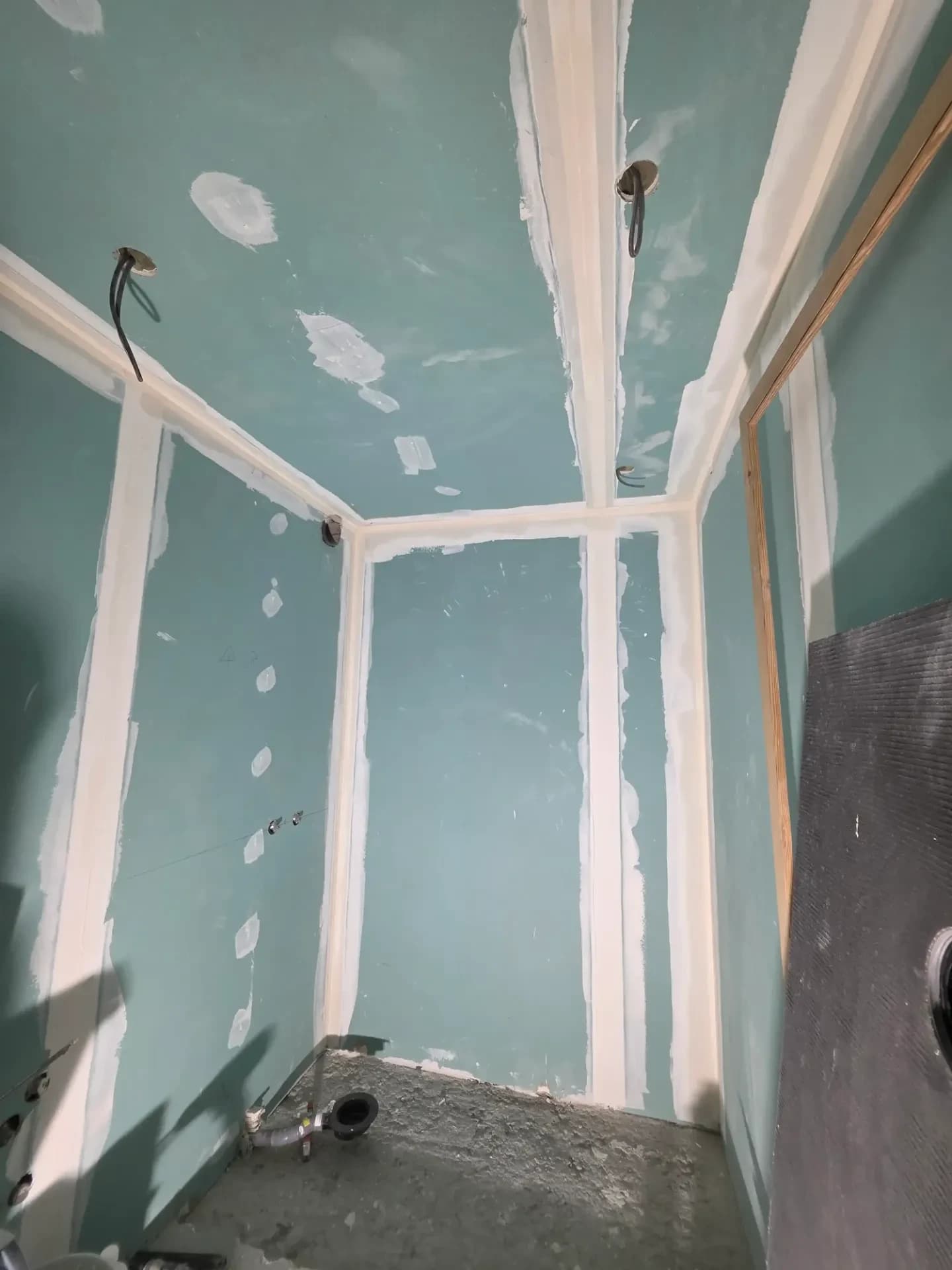 Salle de bain intérieure : cloisons plaquées, joints blancs, câbles et trous, enduit en cours sur murs.