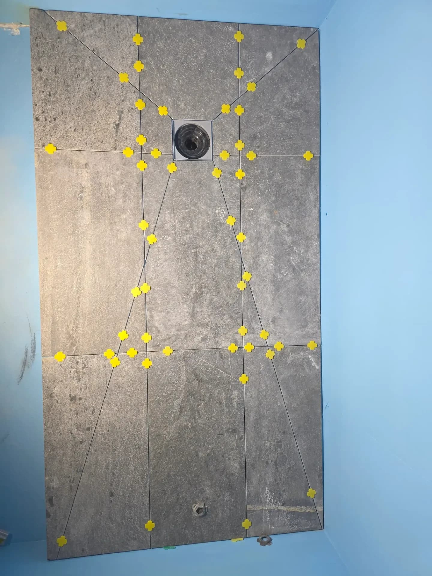 Carreaux effet ardoise et croisillons jaunes, encadrant la bonde d'évacuation du receveur.