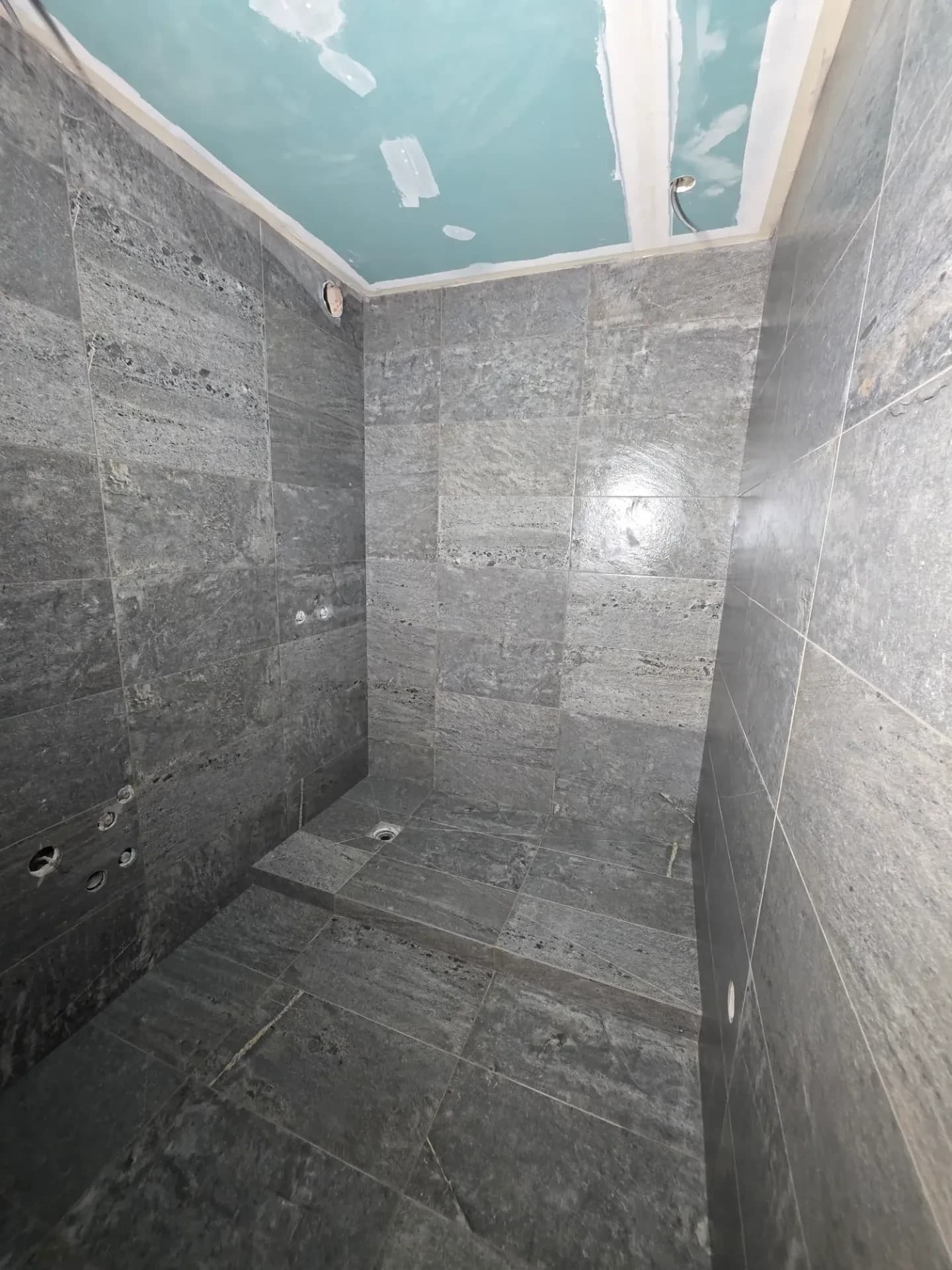 Douche à l’italienne en carrelage gris, sol drainant, murs en pierre, plafond placo.