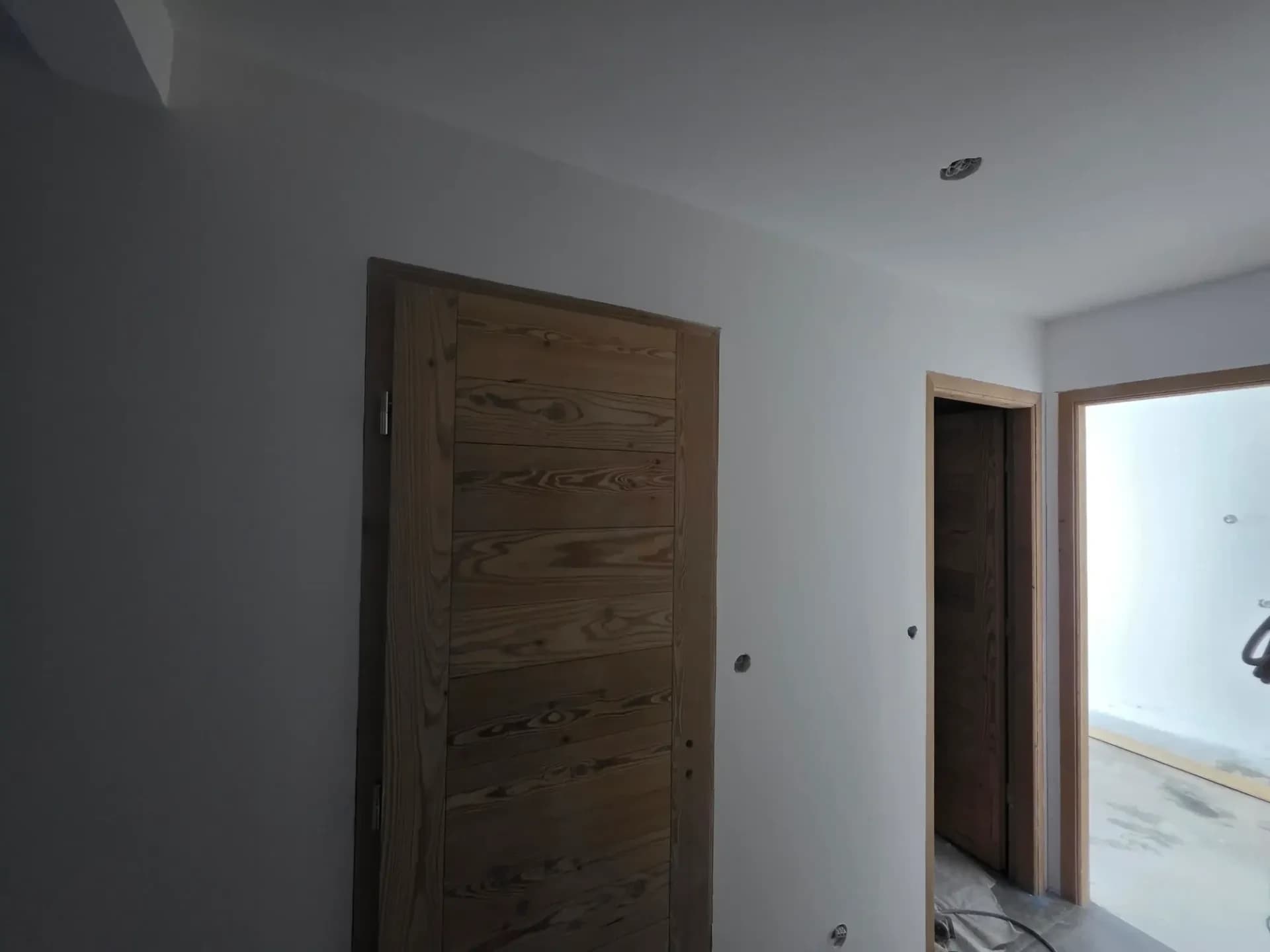 Intérieur en rénovation, portes en bois mélèze et murs blancs, plafond enduit.