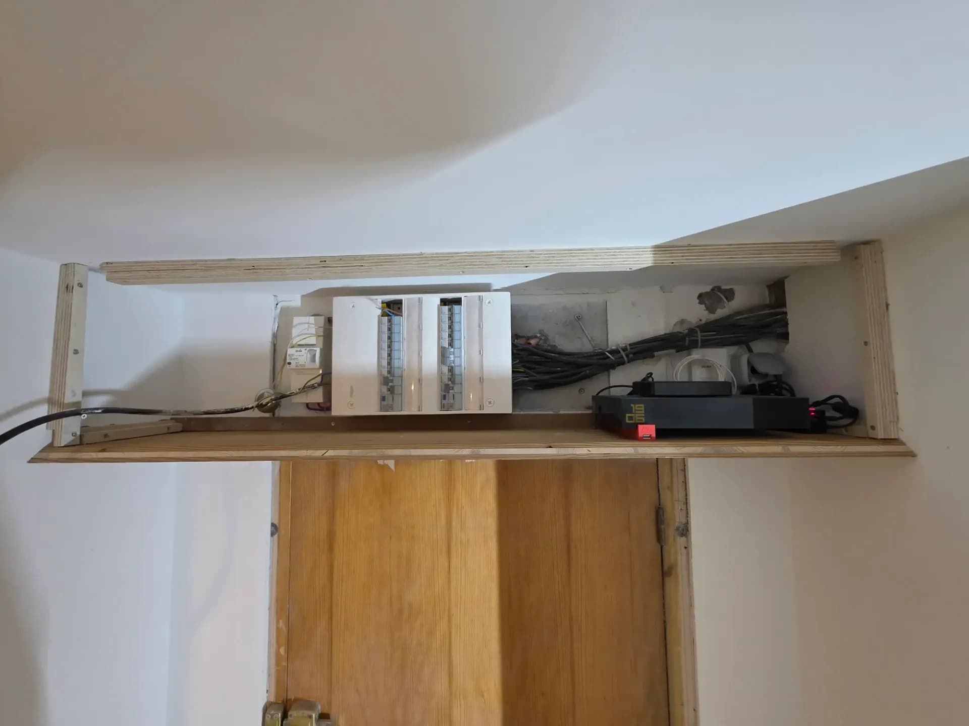 Coffret électrique encastré ouvert dans un caisson en bois fabriqué par l'entreprise de rénovation général, câbles et modules visibles.